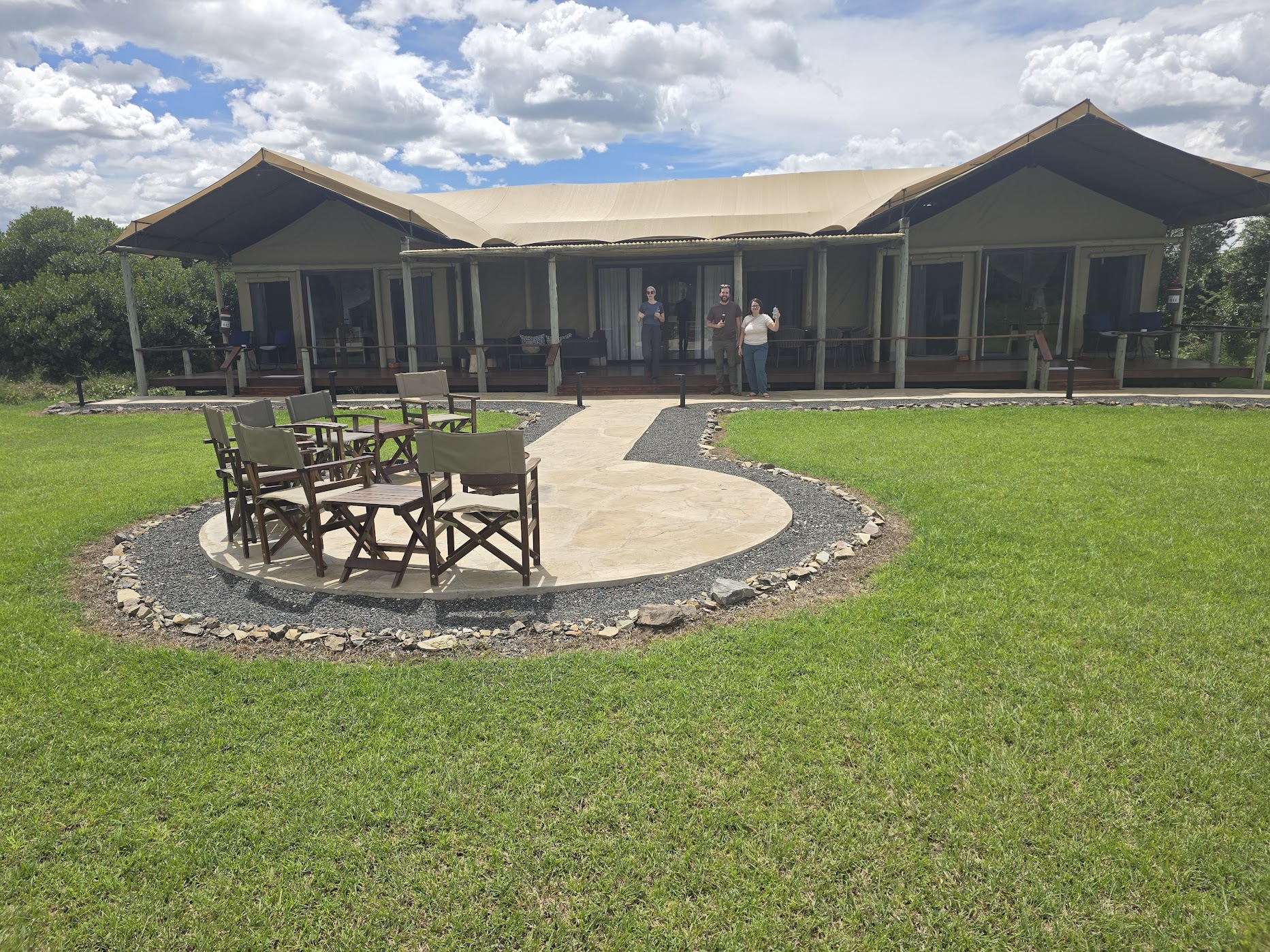 A private two-bedroom tented safari villa at Ol Pejeta with a wide canvas-and-corrugated roof and timber deck, fronted by a stone-edged firepit ring of dark wood camp chairs on manicured lawn.