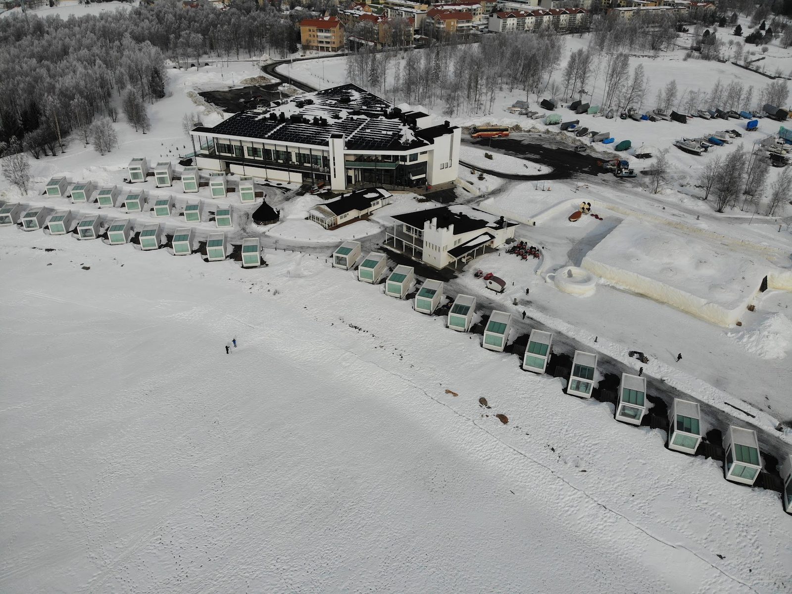 Aerial view of a long row of white glass-roofed seaside villas lined along a frozen shoreline beside a modern resort building in Kemi, Finland.