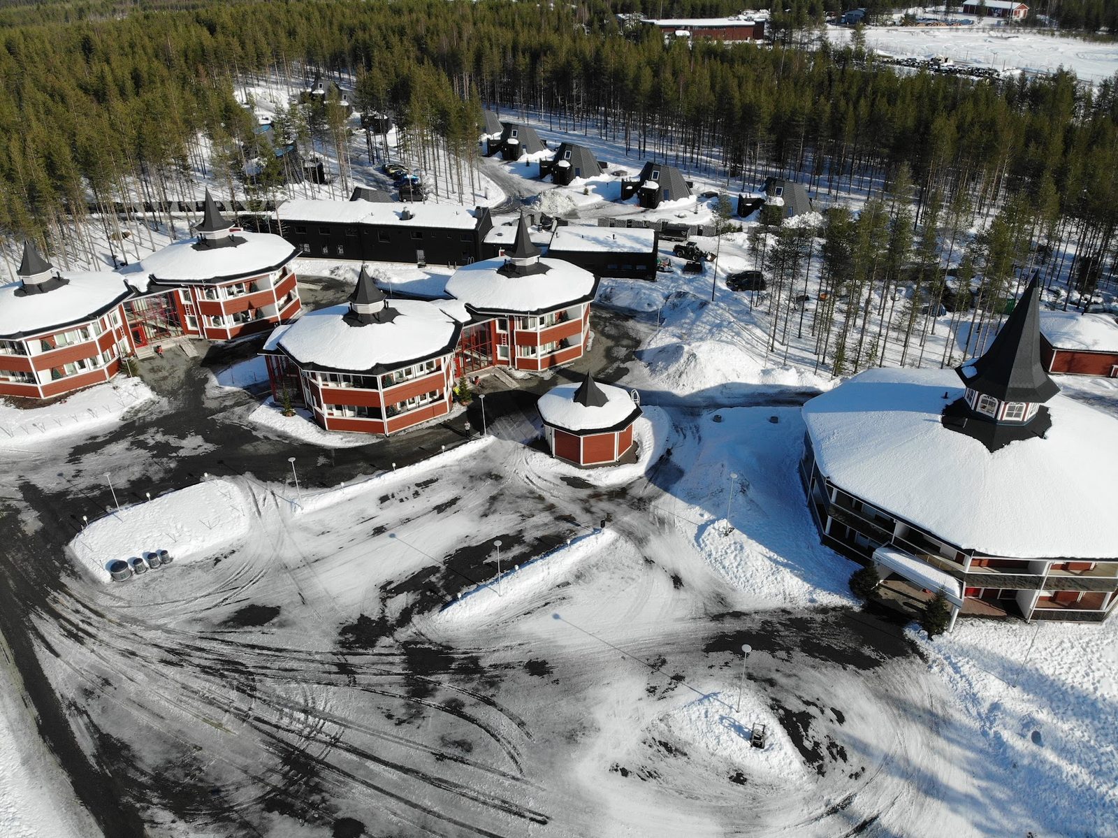 Aerial view of a cluster of red-roofed, turret-topped village hotel buildings ringed by snow-covered pine forest in Rovaniemi.
